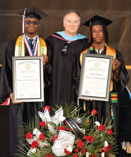 Two students smiling holding diplomas with an administrator