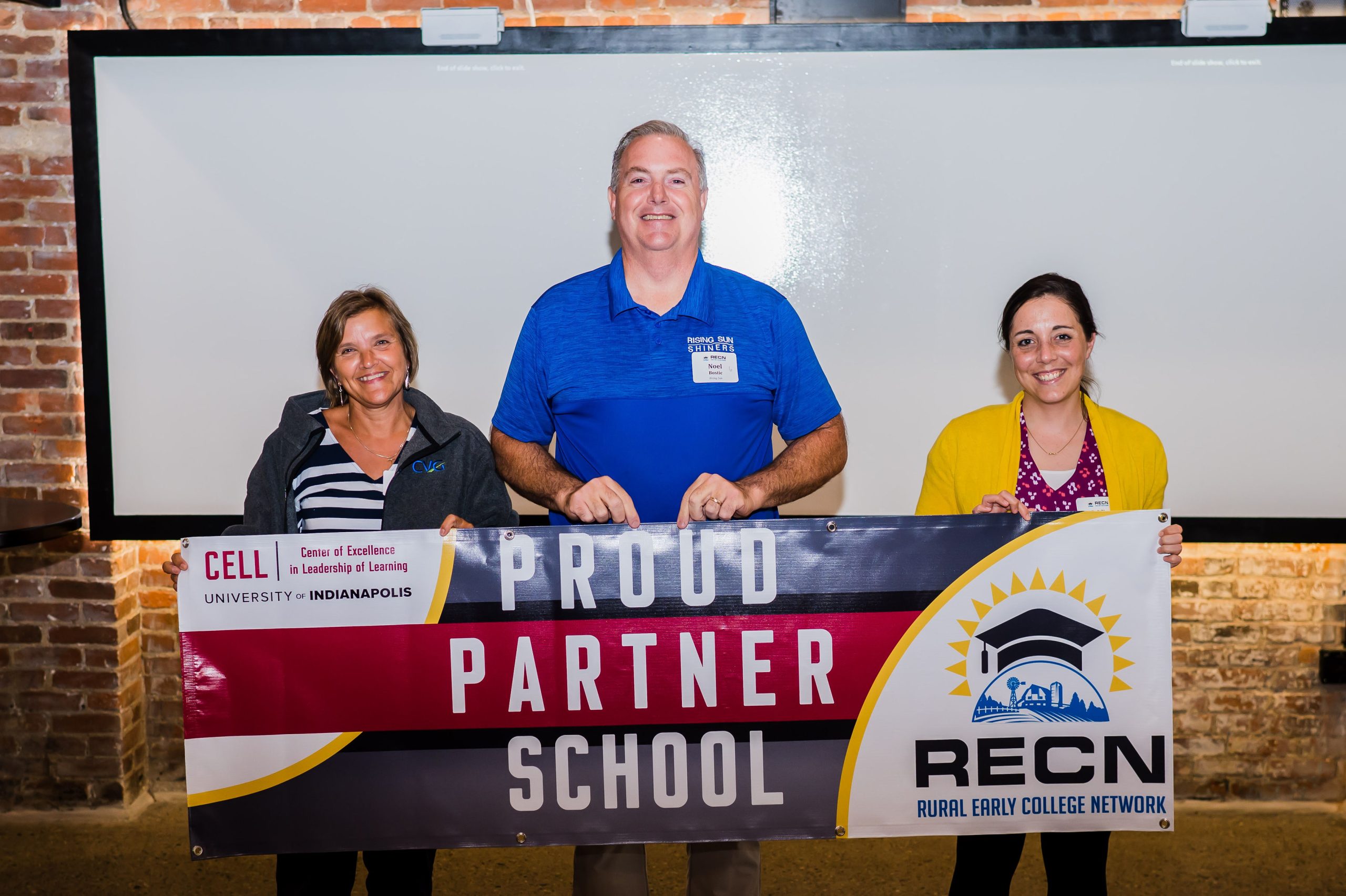 Three people holding banner saying "Proud Partner School"